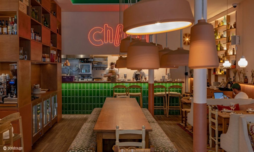 Photo du projet du restaurant le Chocho Paris, par l'architecte d'intérieur Paris, Marjorie Branco. Vue sur les deux grandes tables d'hôtes centrales qui ouvrent la perspective sur la cuisine ouverte.